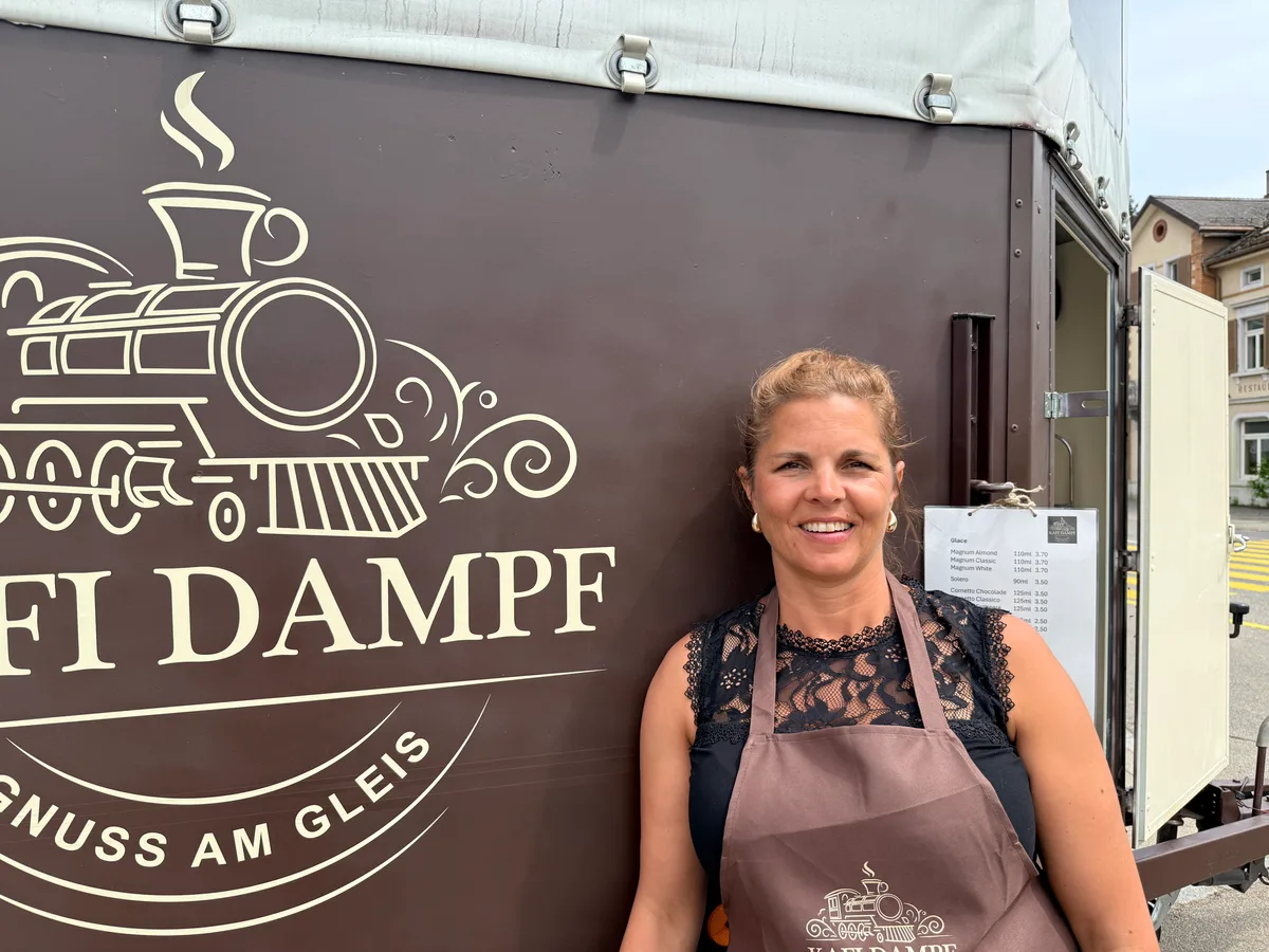 Rahel Straub mit brauner Schürze vor schokoladenbraunem Anhänger mit Dampflok-Logo.